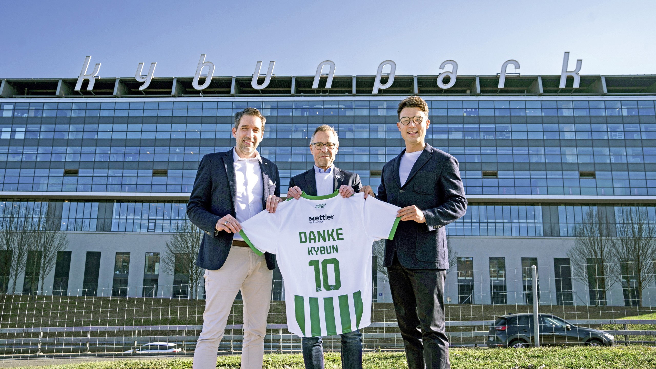 Claudio Minder (l.) und Karl Müller (r.), CEOs der kybun Joya Gruppe mit FCSG Präsident Matthias Hüppi vor der 70 Meter langen Leuchtreklame, welche das Stadion schmückt. Sie gehört laut Aussage von Minder mit 250 000 Franken zu den teuersten Leuchtreklamen der Schweiz.